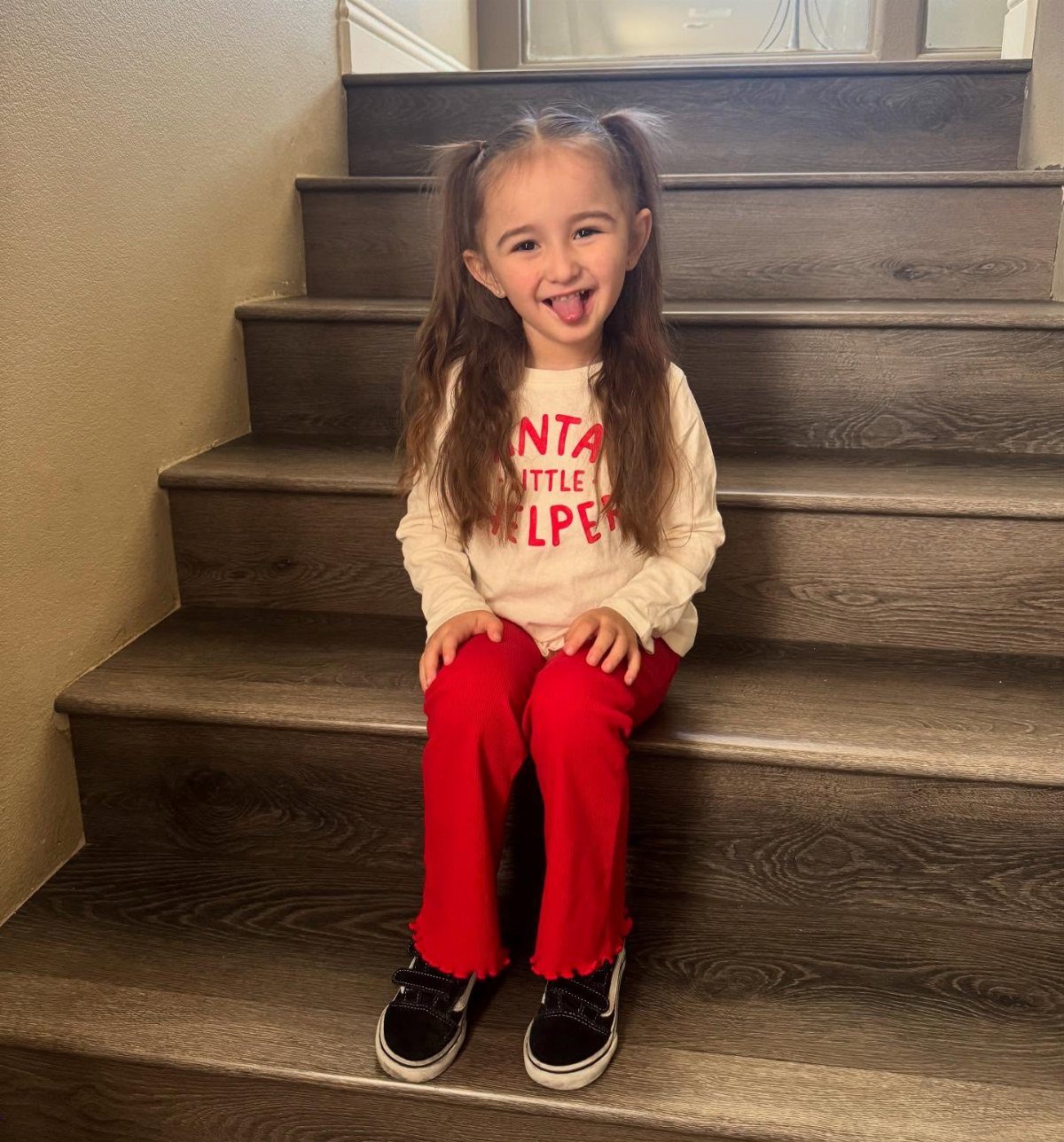 Young girl in a Santa's little helper shirt and red pants on stairs.