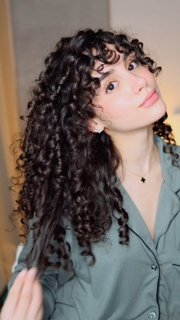 Woman with long dark defined curls and curly bangs wearing a green shirt