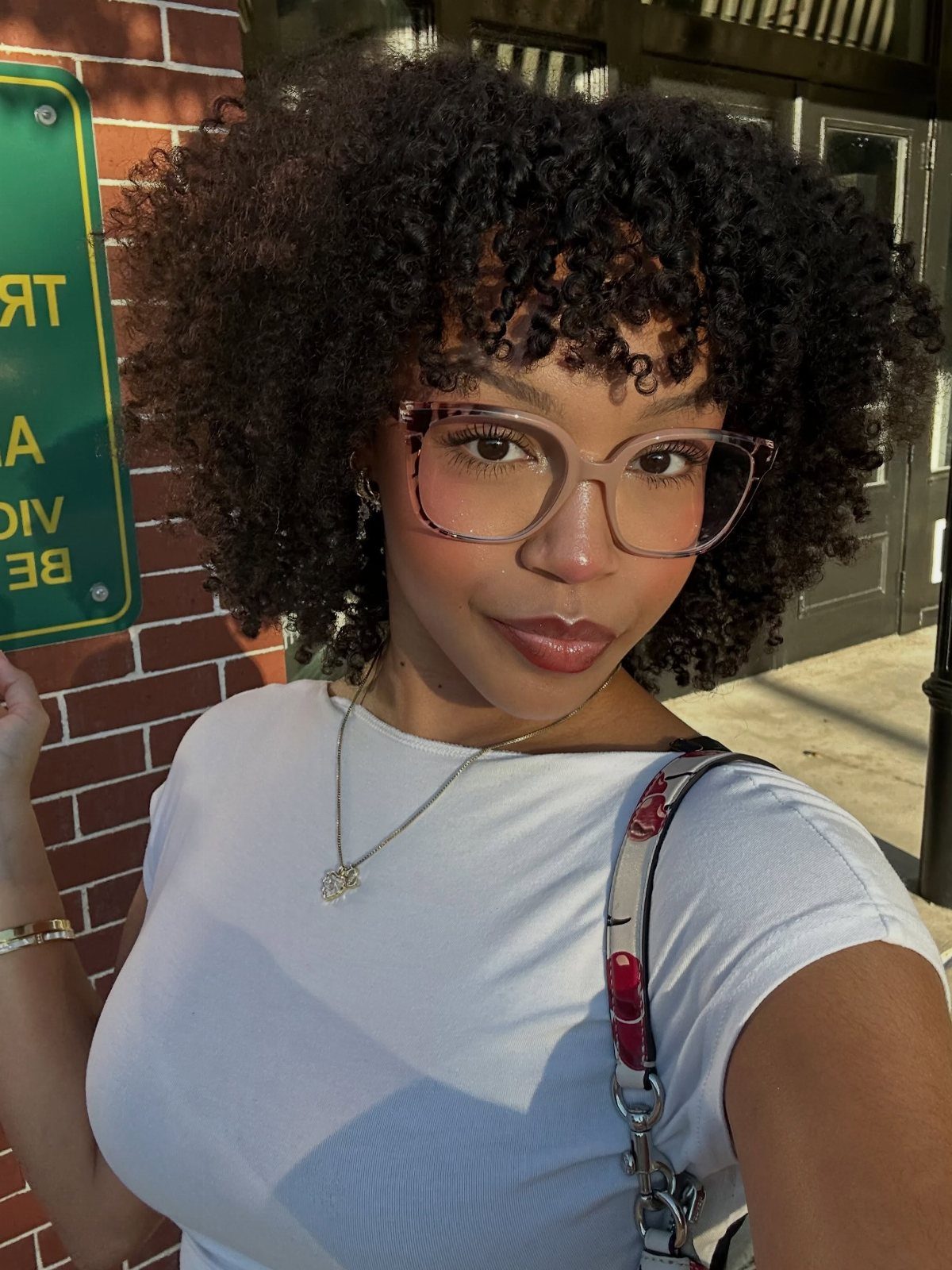 Woman with voluminous dark curly hair wearing glasses and a white t-shirt.