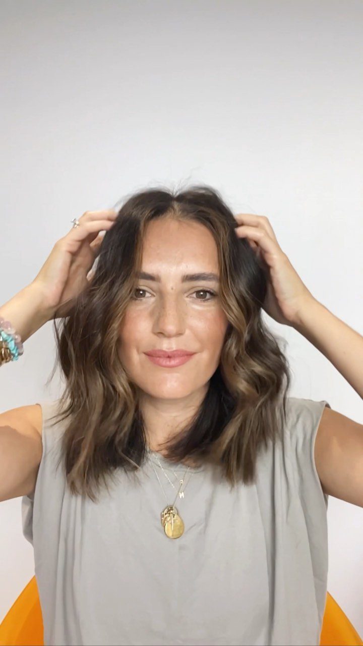 Woman with a wavy brown lob hairstyle posing against a white background.