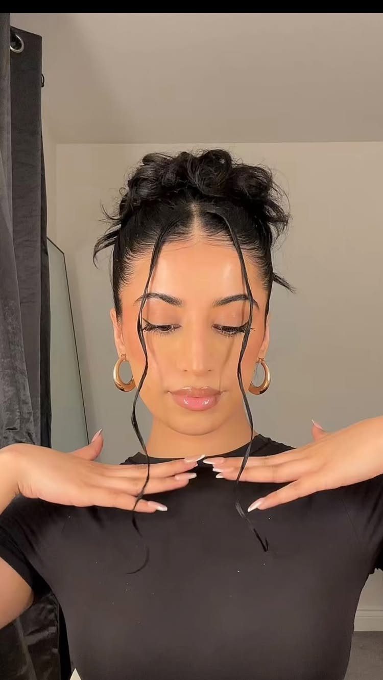 Woman with a high curly bun and long face-framing tendrils wearing gold earrings.