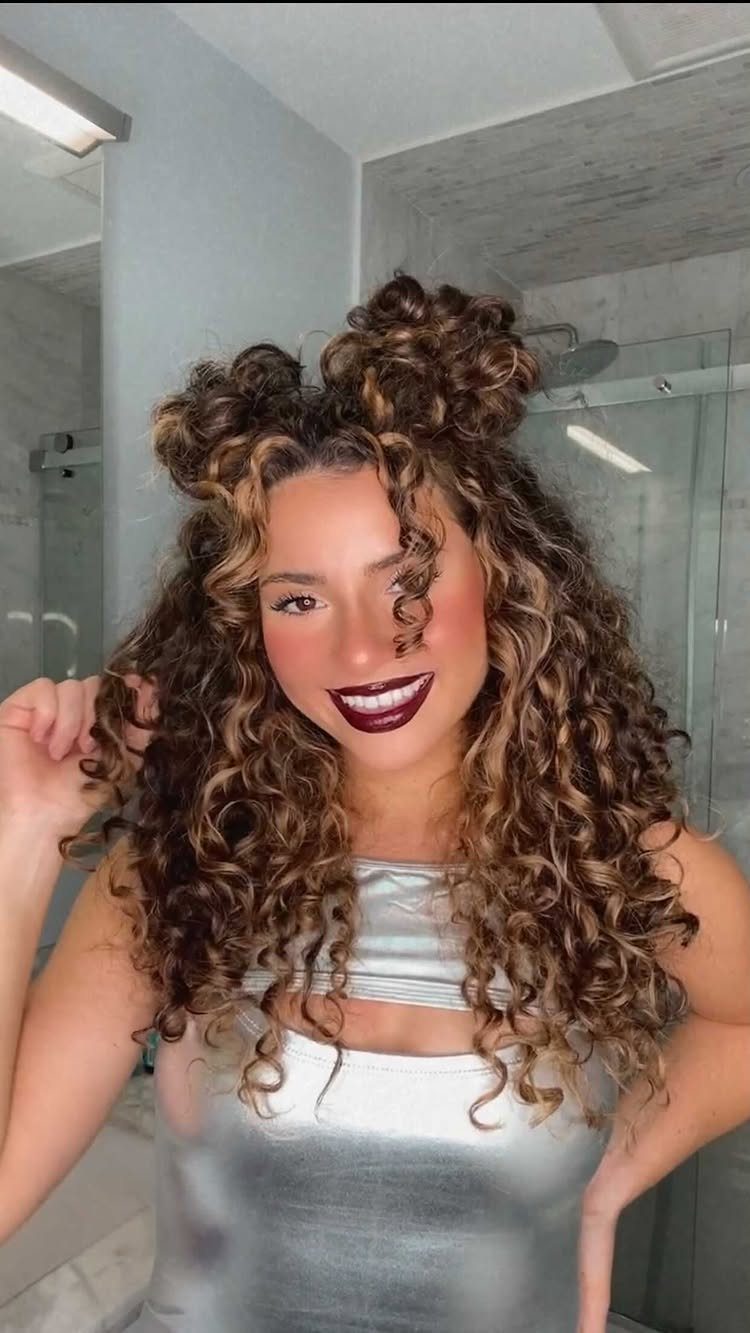 Woman with curly brown hair styled in two high space buns and loose curls.
