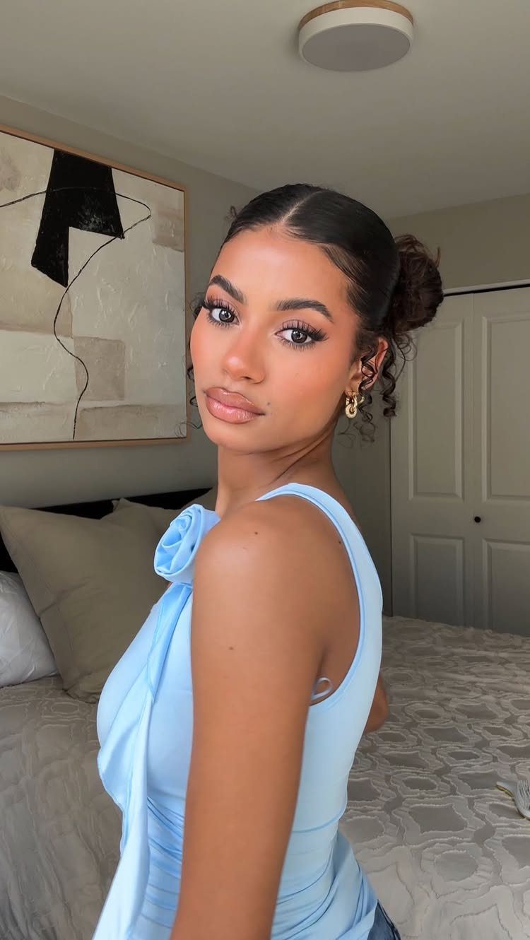 Woman with dark hair in a high curly bun wearing a blue dress