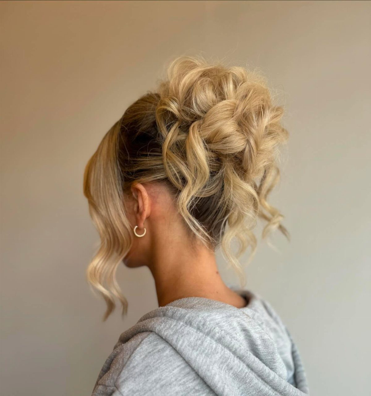 Blonde woman with a messy curly bun and a loose face-framing strand.