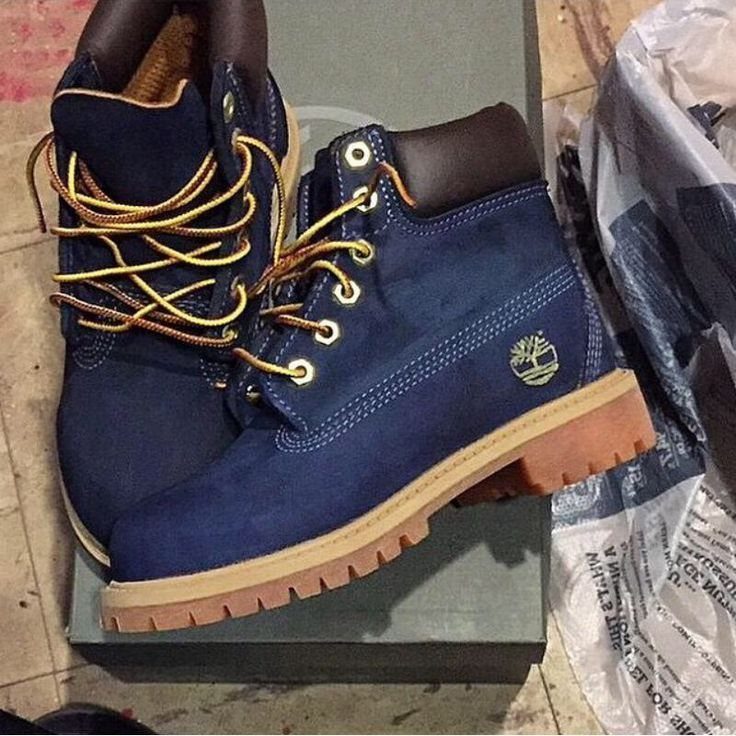 Dark blue Timberland boots with yellow laces resting on a grey shoebox.