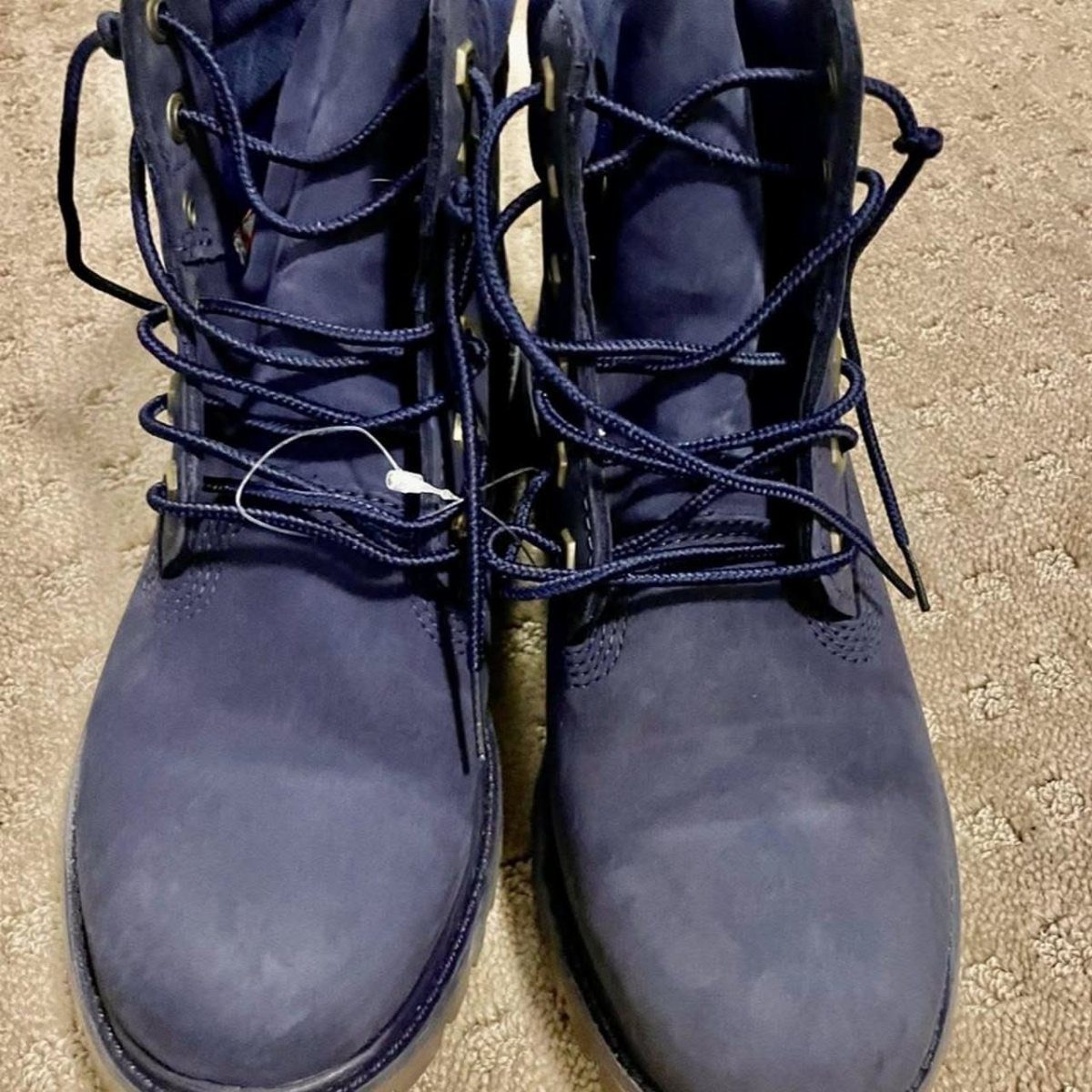 Dark blue nubuck ankle boots with matching laces on a beige carpet.