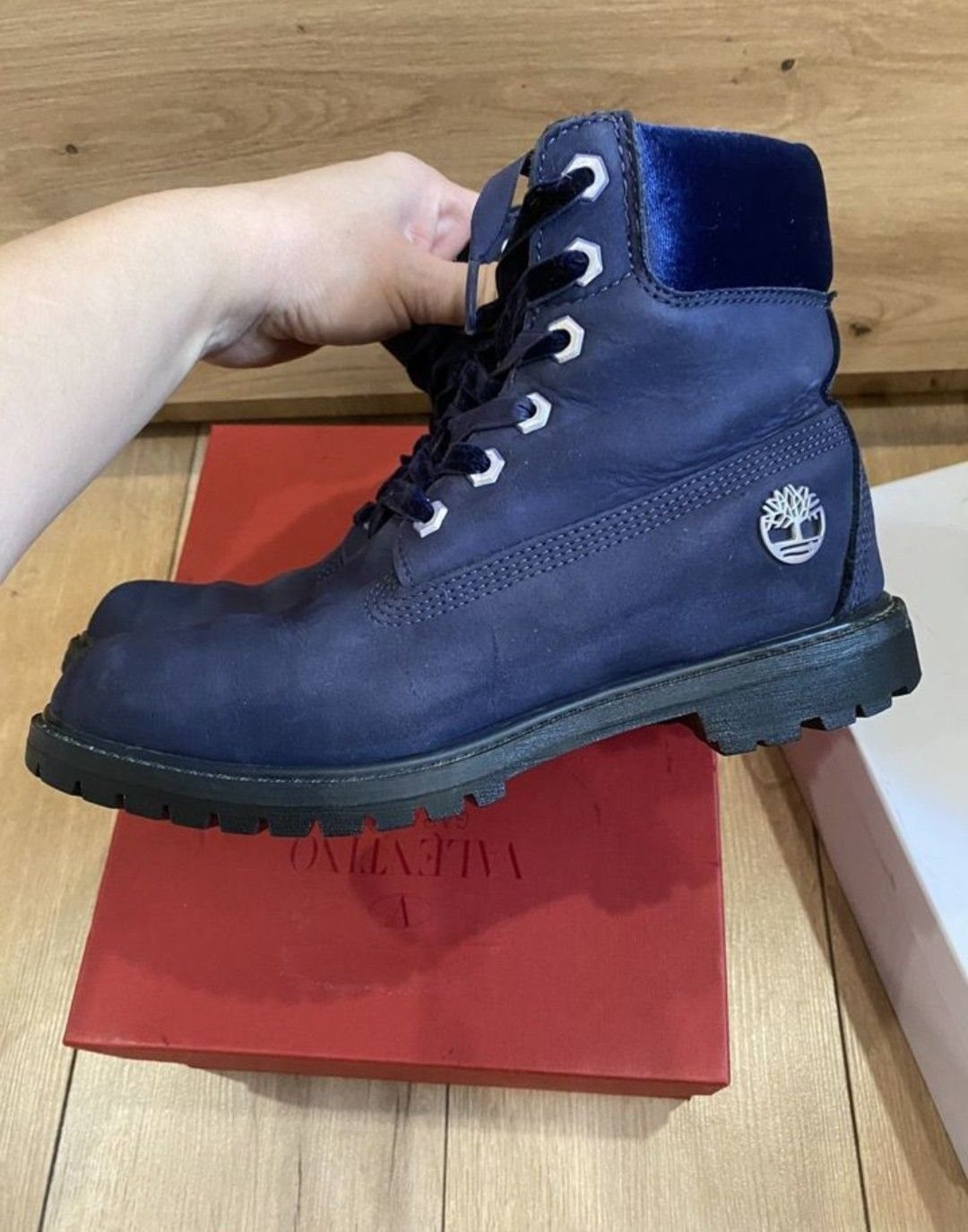 Dark blue Timberland boot held by a hand over a red shoebox.