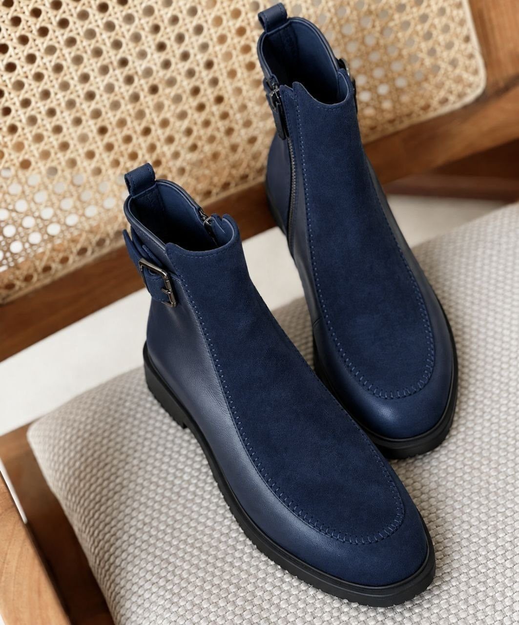 Navy blue nubuck and leather ankle boots resting on a grey fabric chair.