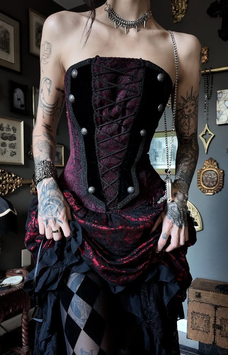 Person wearing a burgundy velvet corset with a red patterned skirt and tattoos.