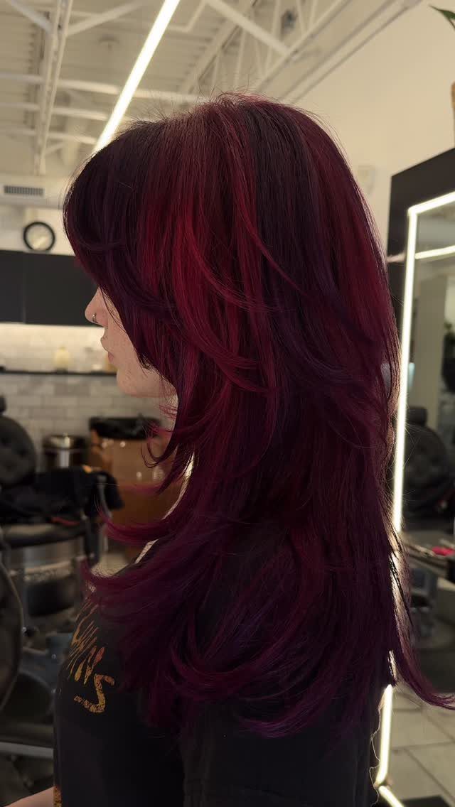 Long layered dark violet hair with sweeping bangs in a salon setting.