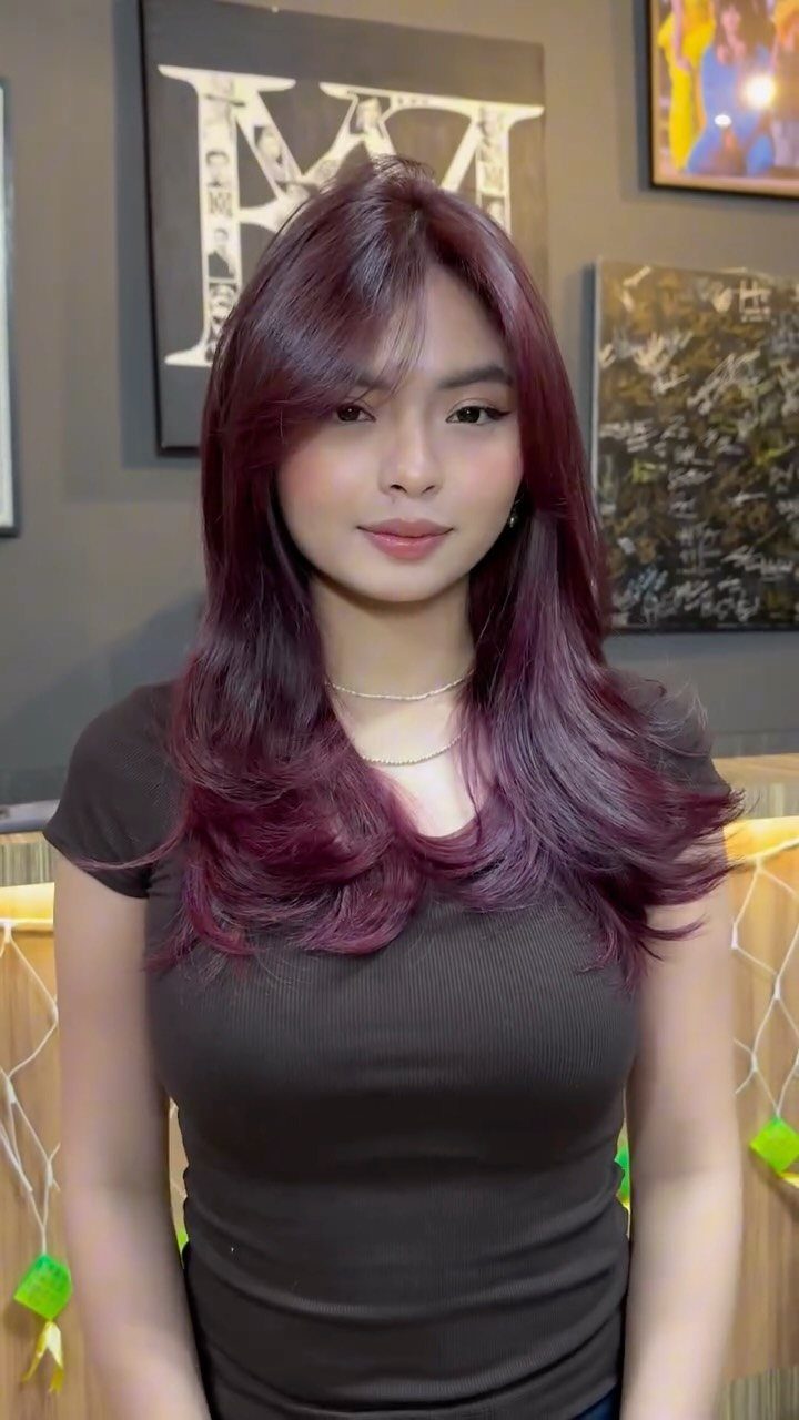 Different Shades of Red Hair Dye: 15 Looks, Copper to Crimson 1 Woman with long wavy burgundy hair wearing a dark brown t-shirt indoors.