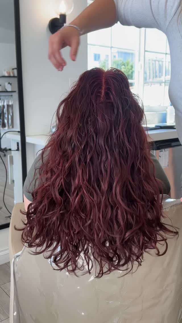Different Shades of Red Hair Dye: 15 Looks, Copper to Crimson 14 Long curly wine-red hair shown from behind in a bright hair salon setting.