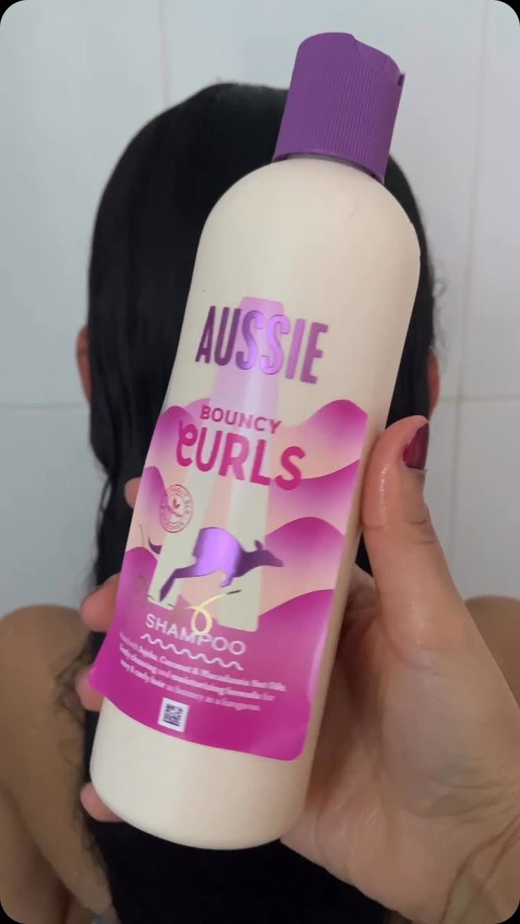 Aussie Bouncy Curls shampoo bottle held in front of a person with dark hair.