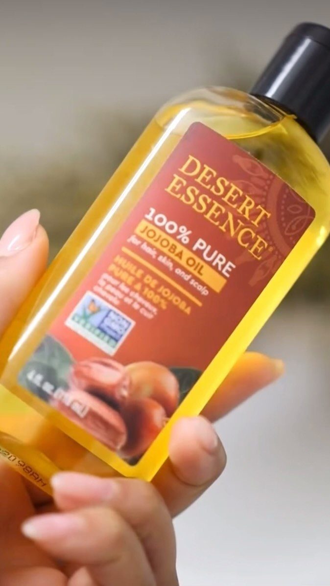 Hand holding a bottle of Desert Essence Pure Jojoba Oil for hair and skin