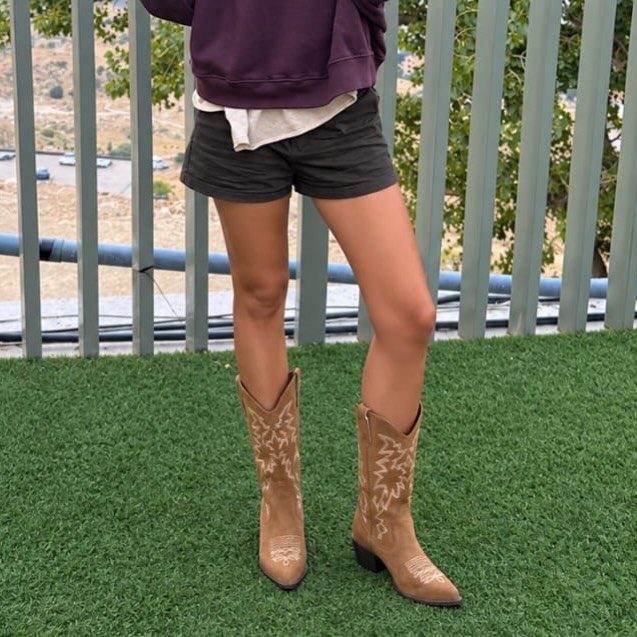 Fall Cowboy Boots for Women: 9 Ideas to Wear Now 9 Tan cowboy boots with white embroidery worn with dark shorts on green turf.