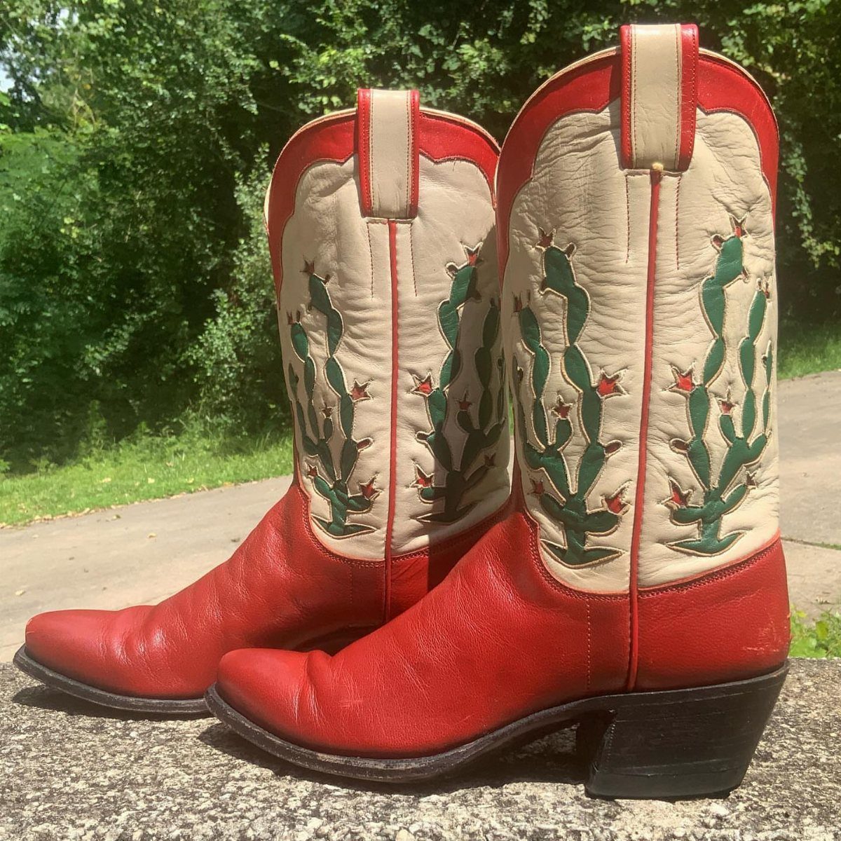 Fall Cowboy Boots for Women: 9 Ideas to Wear Now 5 Red and white cowboy boots with green cactus embroidery on a concrete ledge.