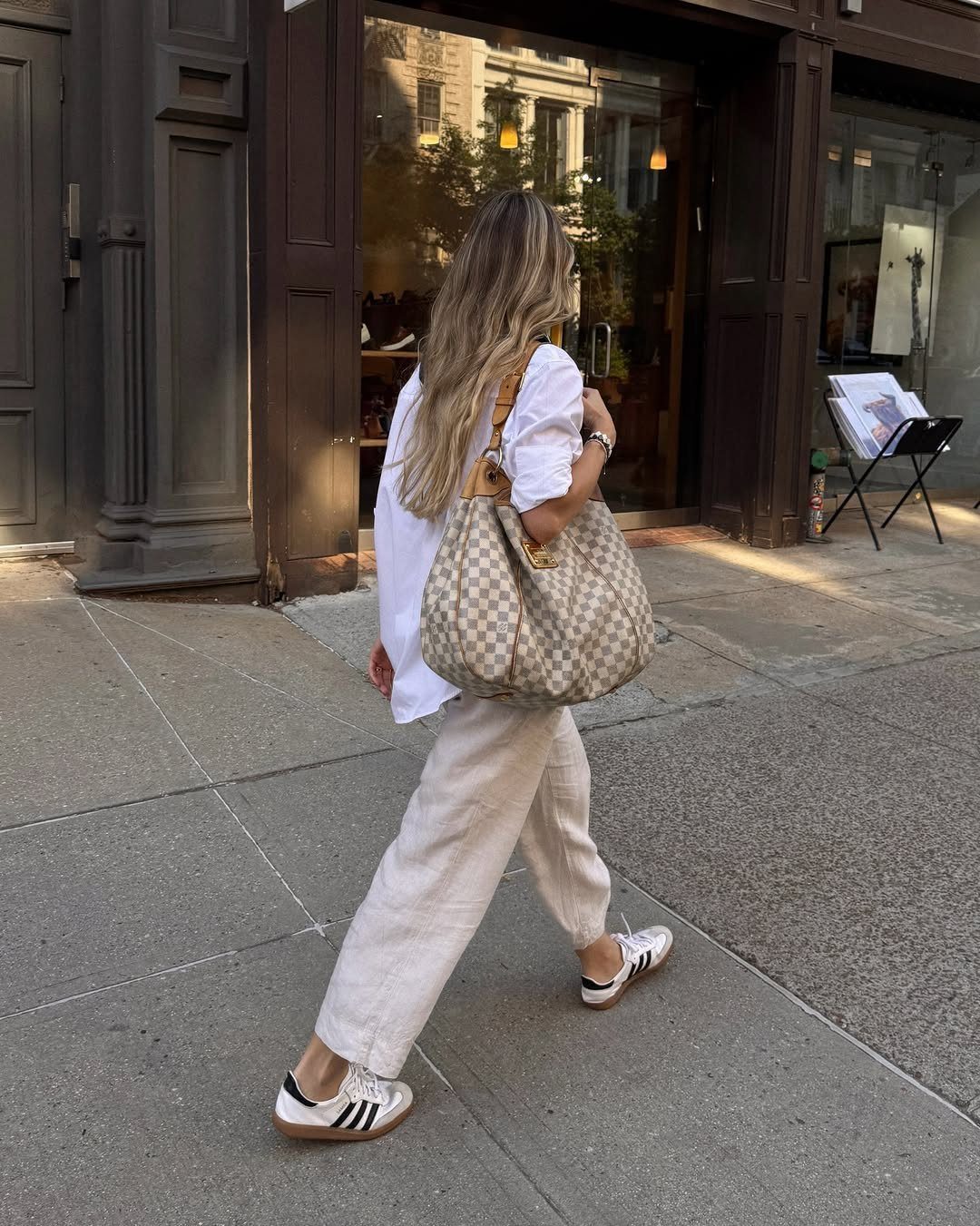 Fancy Sneakers for Women: 9 Ideas, From Retro to Platform 9 Woman walking on sidewalk wearing white Adidas Samba sneakers and cream trousers