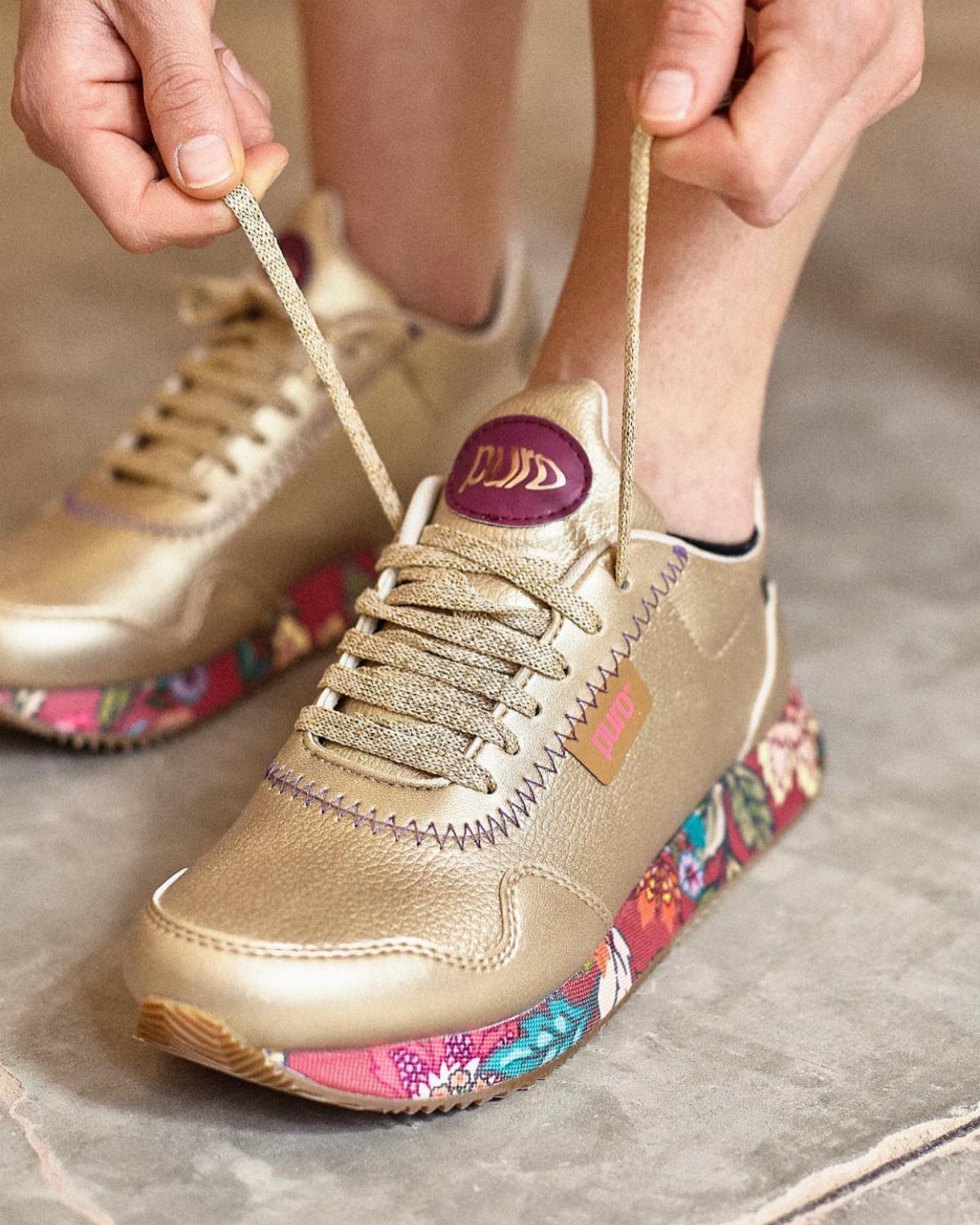 Fancy Sneakers for Women: 9 Ideas, From Retro to Platform 1 Metallic gold sneakers with floral midsoles being laced up by a person's hands.