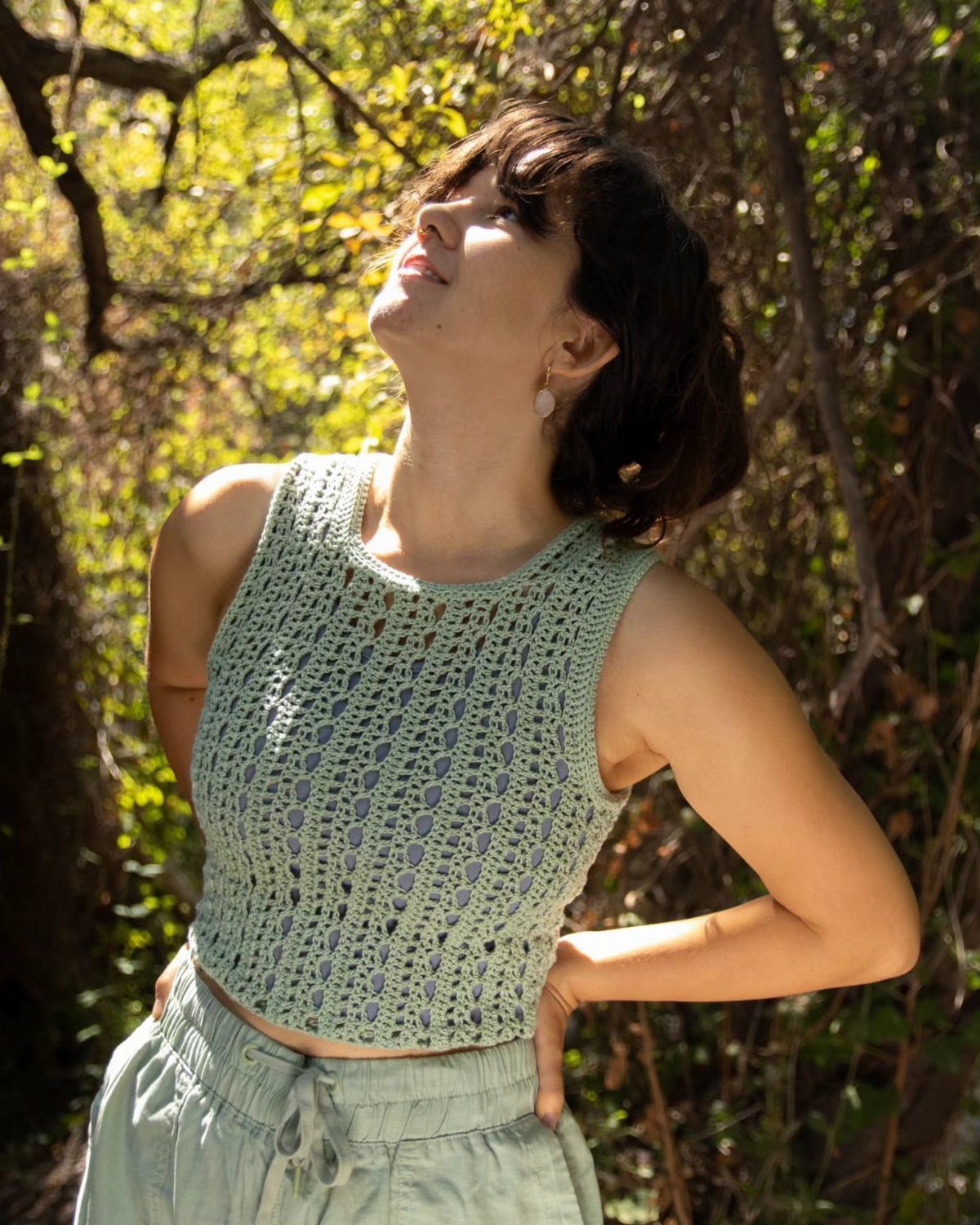 Gillian Practical Magic Outfits: 11 Ideas to Wear Now 9 Woman wearing a light green crochet crop top and linen pants in woods