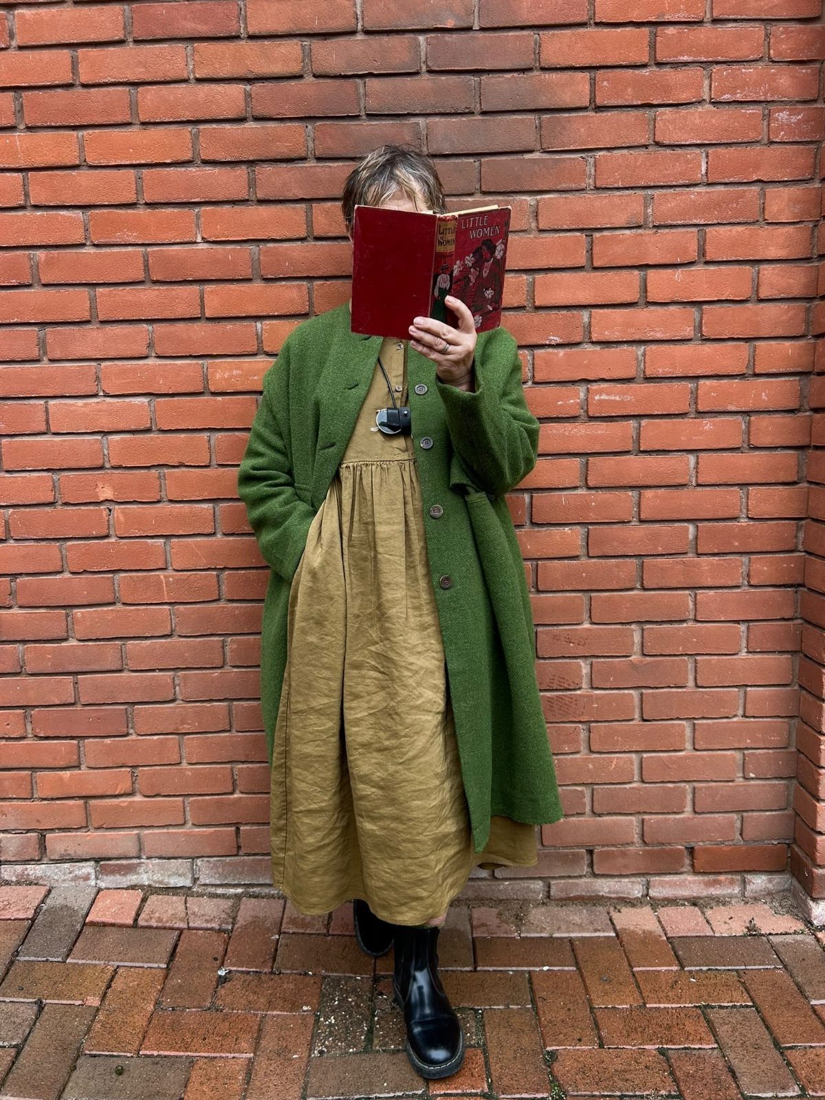 Gillian Practical Magic Outfits: 11 Ideas to Wear Now 11 Person in olive green cardigan and mustard dress holding a red book.
