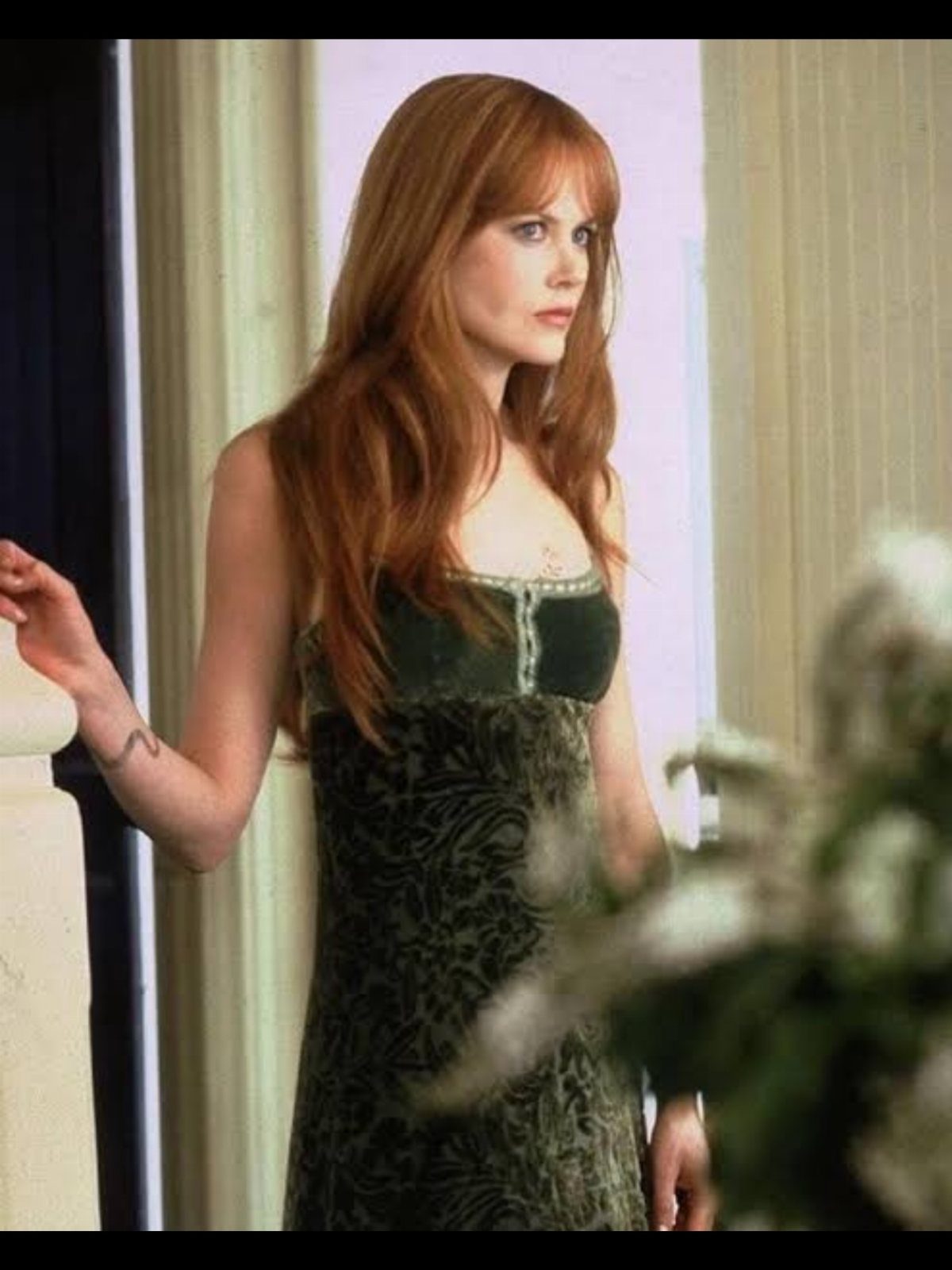 Gillian Practical Magic Outfits: 11 Ideas to Wear Now 1 Woman with red hair wearing a dark green velvet midi dress indoors.