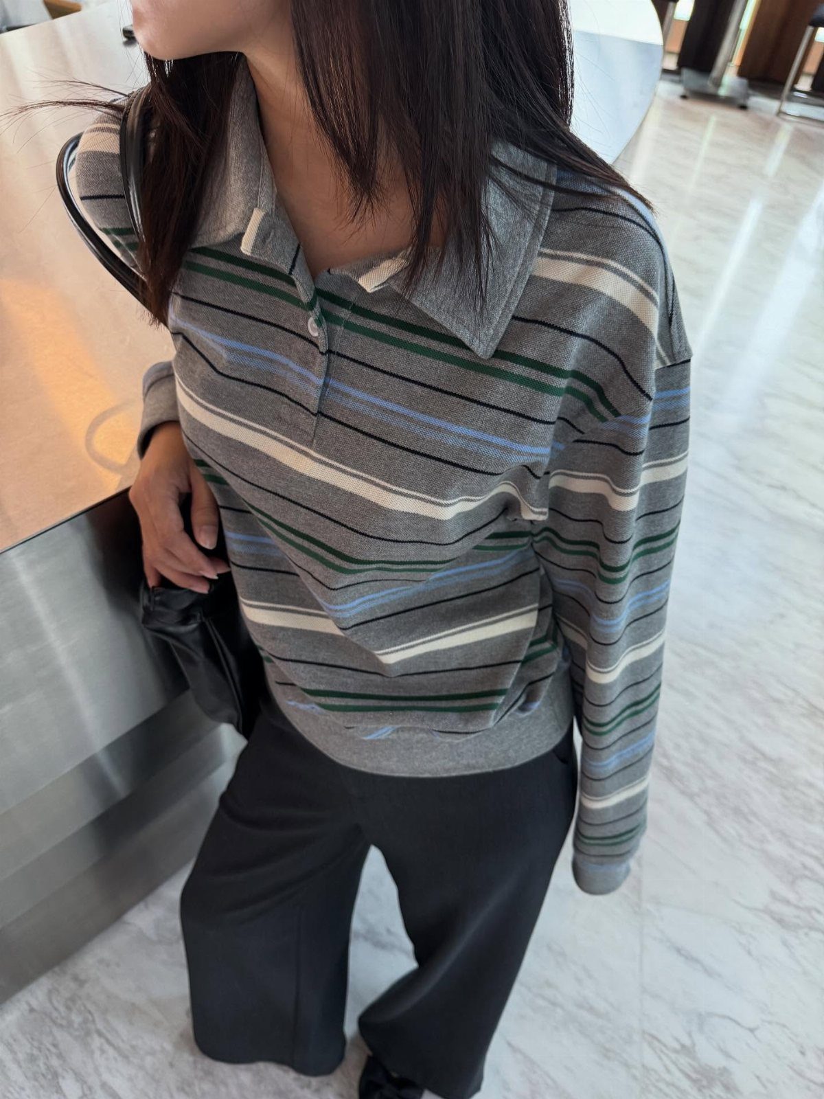 Person wearing a gray striped polo shirt and black wide-leg trousers indoors.