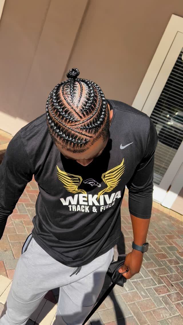 Man with curved cornrow braids tied into a small bun on top.
