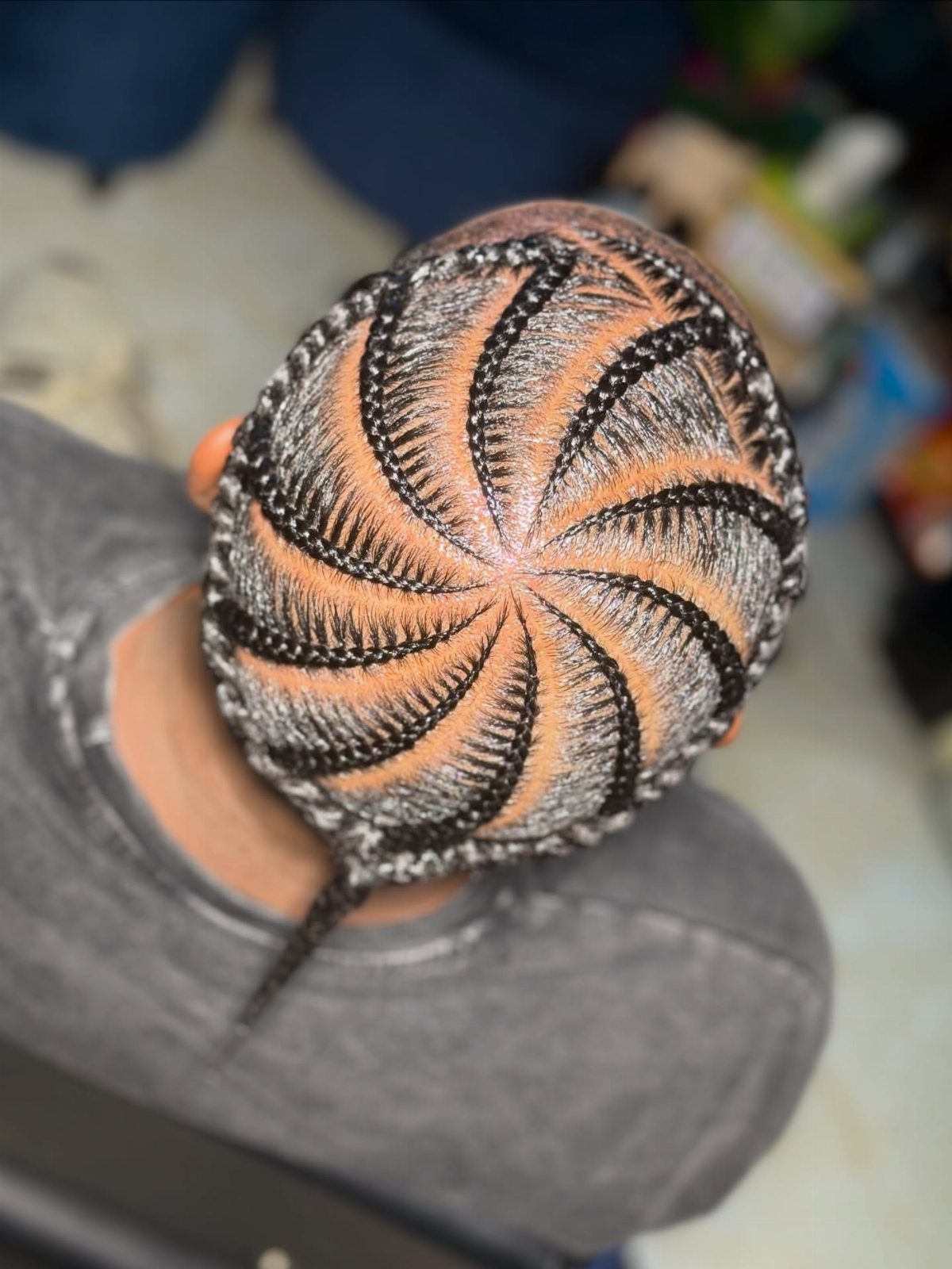 Man's head with black hair braided into a swirling circular cornrow pattern.