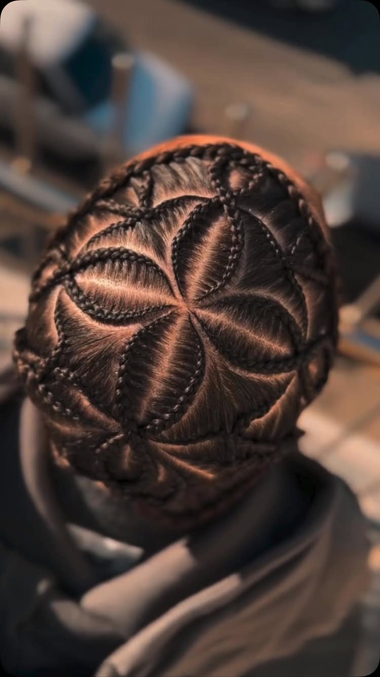 Man's head with intricate geometric cornrow braids forming a flower pattern.