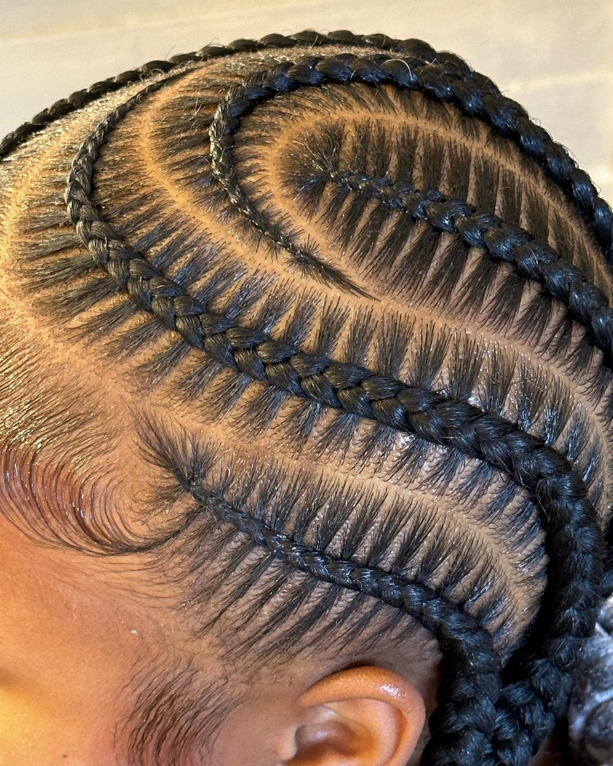 Curved stitch braids on a person's head with precise horizontal parting lines.