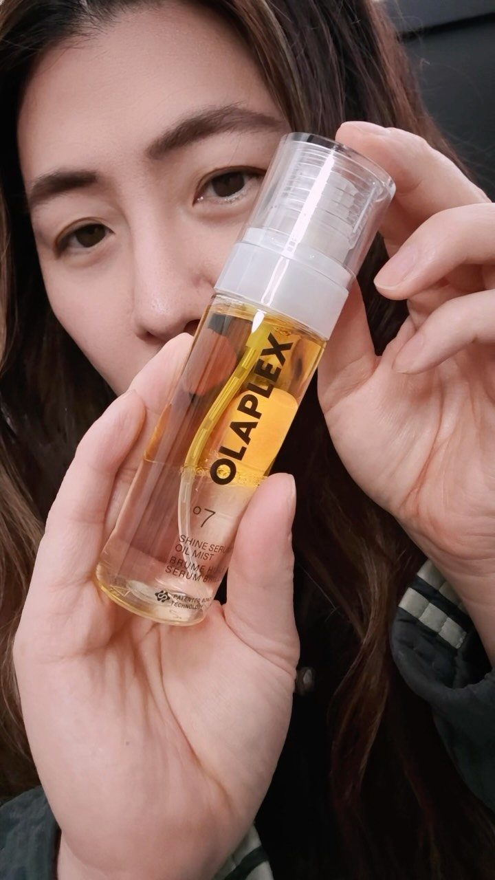 Woman holding a bottle of Olaplex No. 7 Bonding Oil against her face.