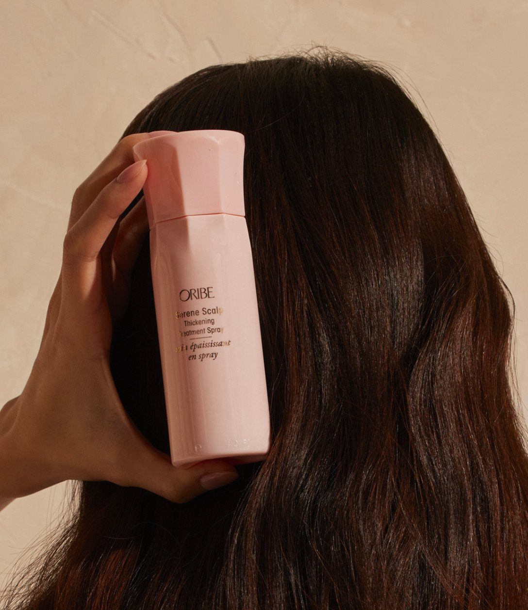 Pink thickening spray bottle held against long, dark brown hair.