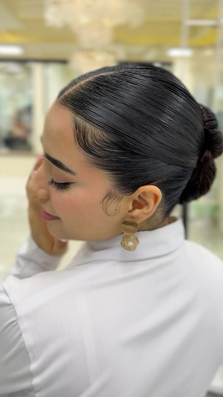 Hair Up Styles to Try: 12 Buns, Ponytails and More 7 Woman with a sleek slicked-back bun hairstyle wearing a white high-neck top.