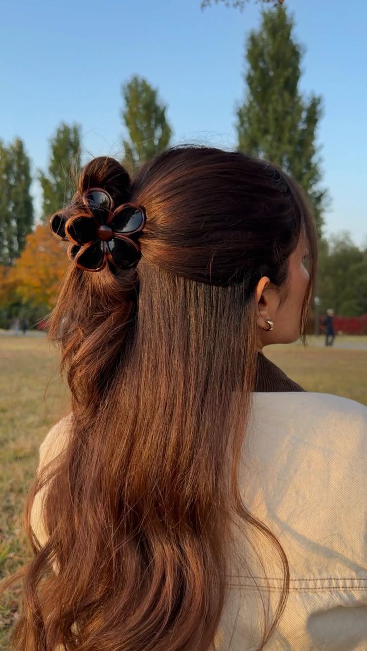 7 Hairstyle for Claw Clip Ideas, Messy Bun to Updo 7 Woman with long brown hair styled with a black flower-shaped claw clip outdoors.