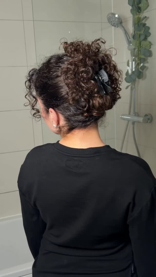7 Hairstyle for Claw Clip Ideas, Messy Bun to Updo 1 Curly brown hair styled in a bun secured with a black claw clip.