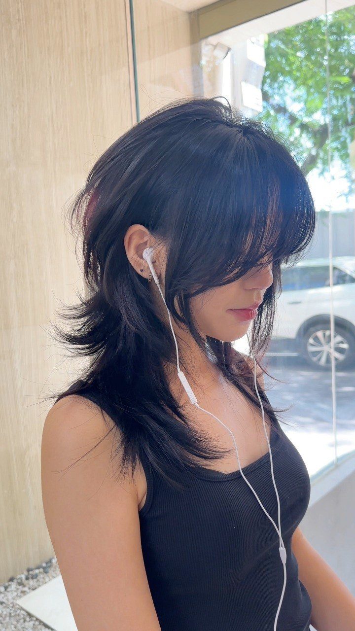 14 Hairstyles for Long Hair for Summer, Easy and Cool 9 Woman with a black layered shag haircut and bangs wearing white wired earbuds.
