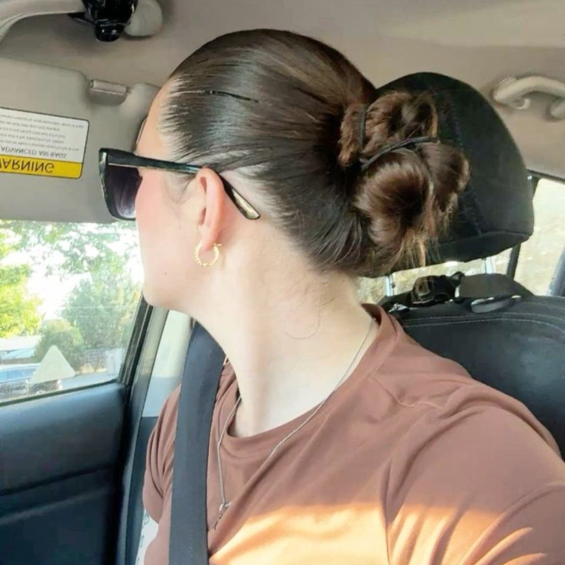 14 Hairstyles for Long Hair for Summer, Easy and Cool 4 Woman with brown hair styled in a low nape knot bun inside a car
