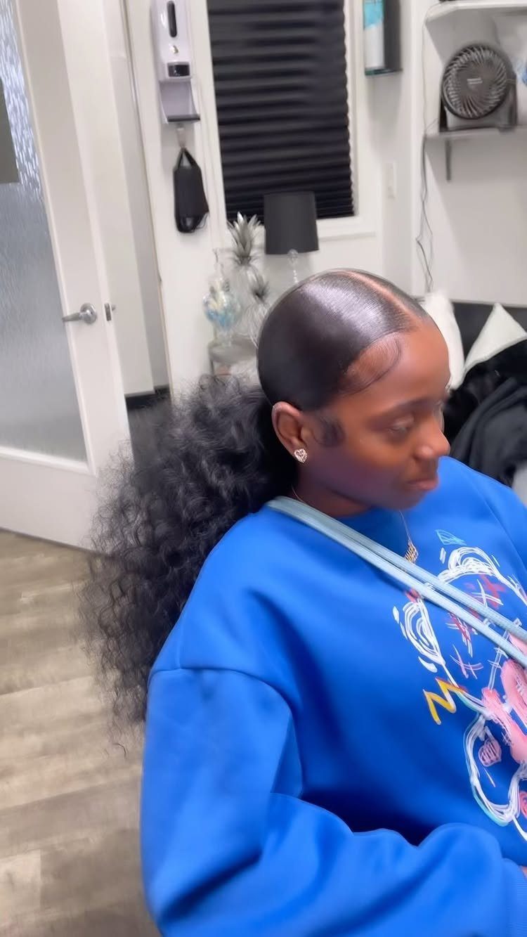 Woman with a sleek slicked-back ponytail and voluminous curly hair in blue sweatshirt