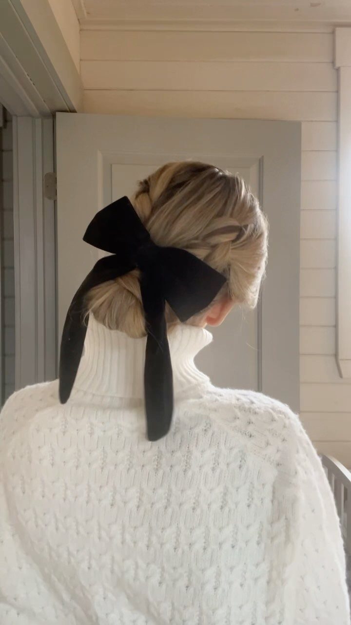 Blonde hair updo with a large black velvet bow and white knit sweater