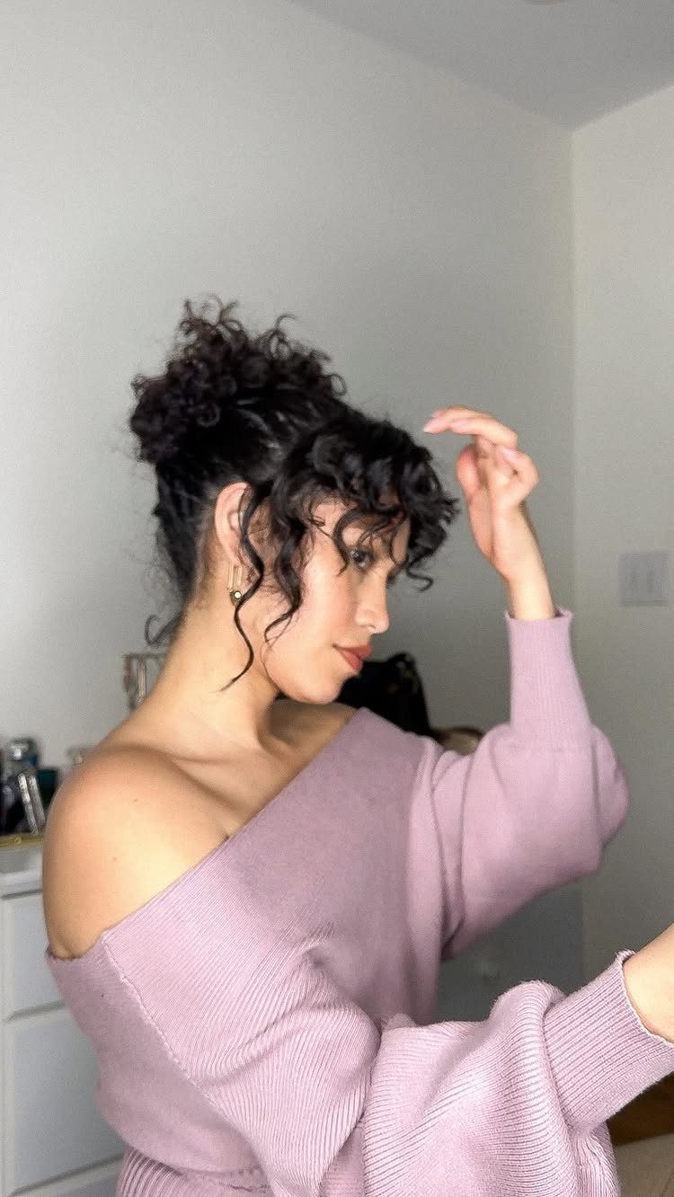 14 Hairstyles with Curly Bangs for Every Length and Curl 10 Woman with dark curly hair in an updo and curly bangs wearing purple sweater
