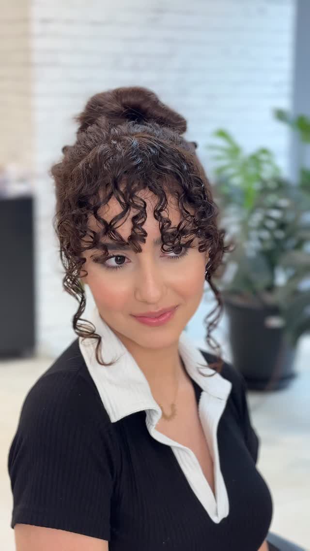14 Hairstyles with Curly Bangs for Every Length and Curl 6 Woman with dark brown hair in a high bun and defined ringlet curtain bangs.