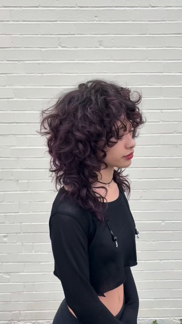 14 Hairstyles with Curly Bangs for Every Length and Curl 4 Person with layered dark brown curly hair and curly bangs against white brick.