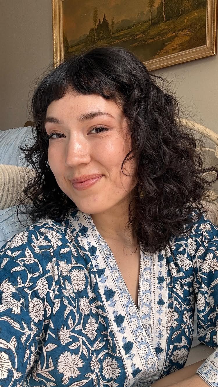 14 Hairstyles with Curly Bangs for Every Length and Curl 14 Woman with dark curly hair and curly bangs wearing a blue floral shirt.