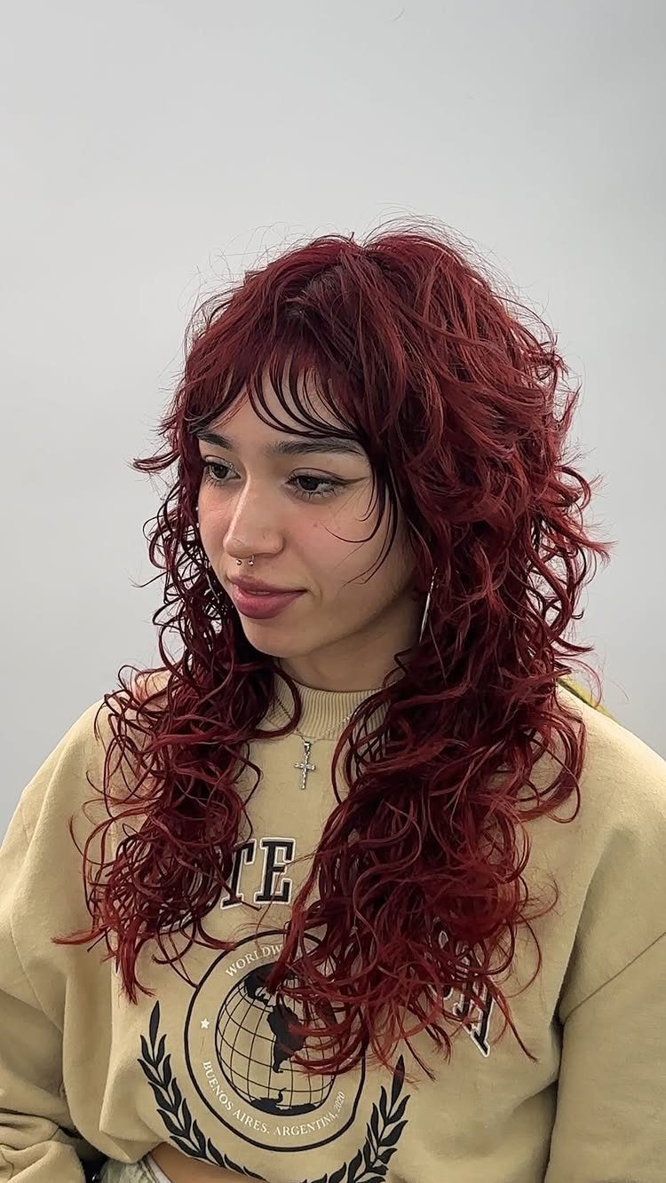 14 Hairstyles with Curly Bangs for Every Length and Curl 1 Woman with long red curly hair and shaggy curly bangs wearing tan sweatshirt.