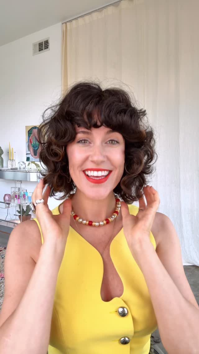14 Hairstyles with Curly Bangs for Every Length and Curl 12 Woman with short curly dark brown hair and curly bangs wearing yellow dress
