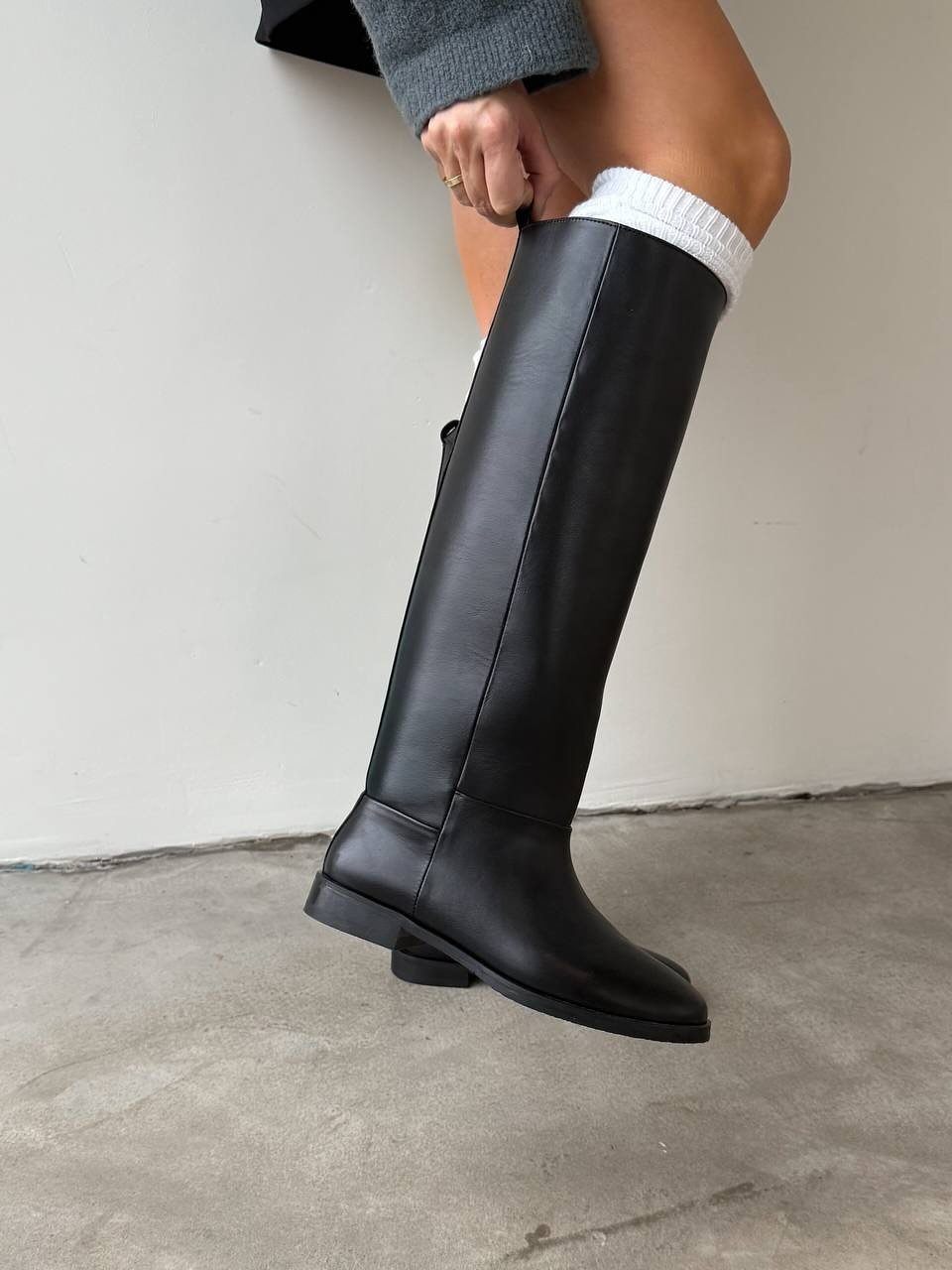 High Cut Boots: 13 Ideas from Kitten Heels to Thigh-High 13 Black leather knee-high boots worn by a person standing against a white wall.