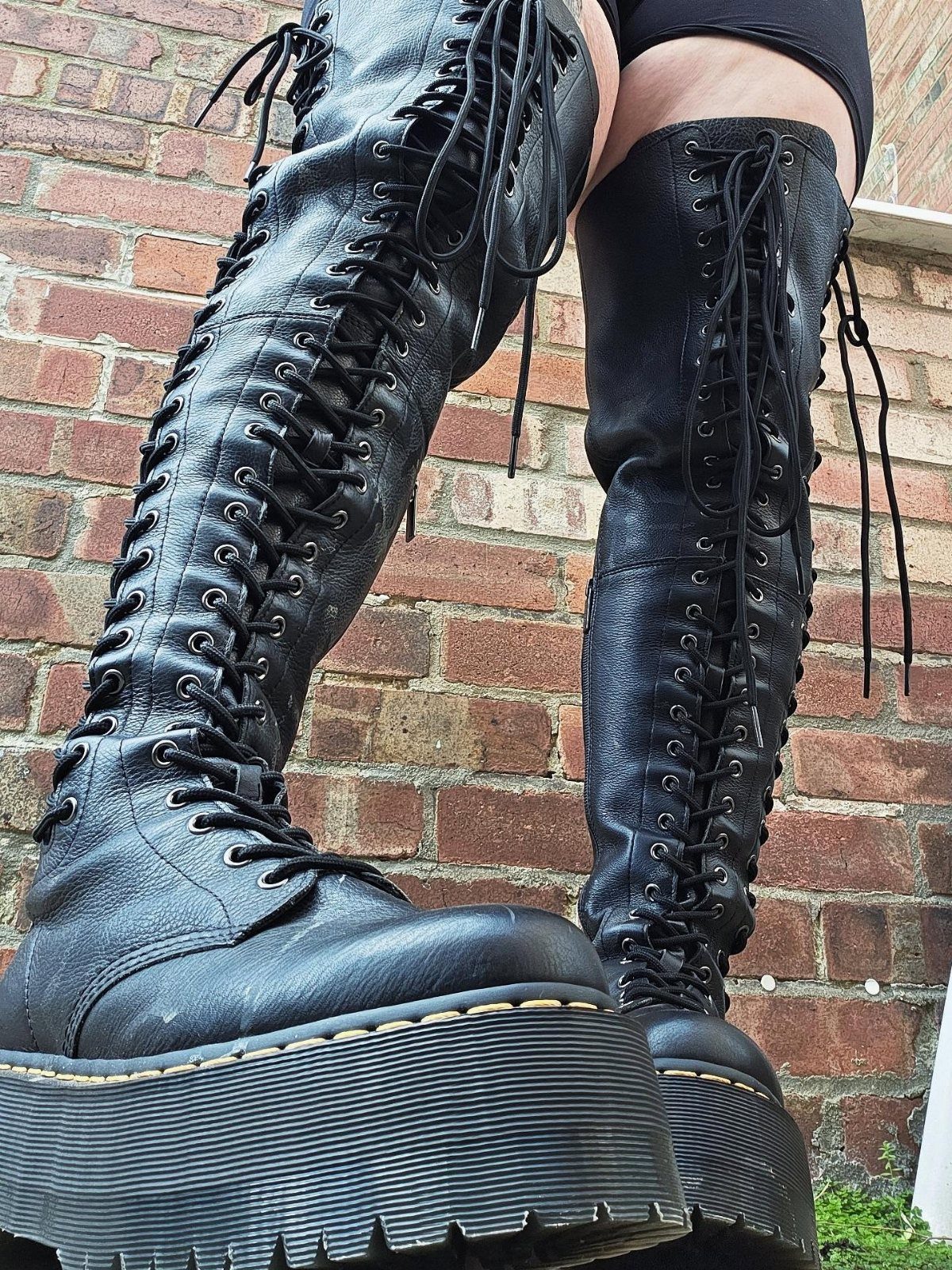 High Cut Boots: 13 Ideas from Kitten Heels to Thigh-High 12 Black leather knee-high lace-up platform boots worn against a red brick wall background.