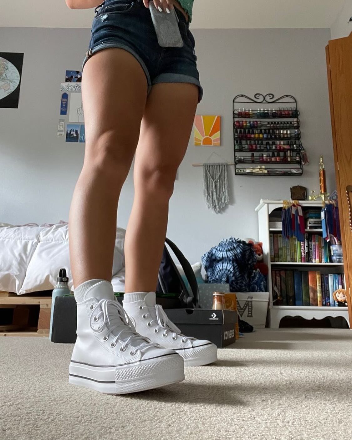 White high-top platform sneakers worn by a person in denim shorts indoors.