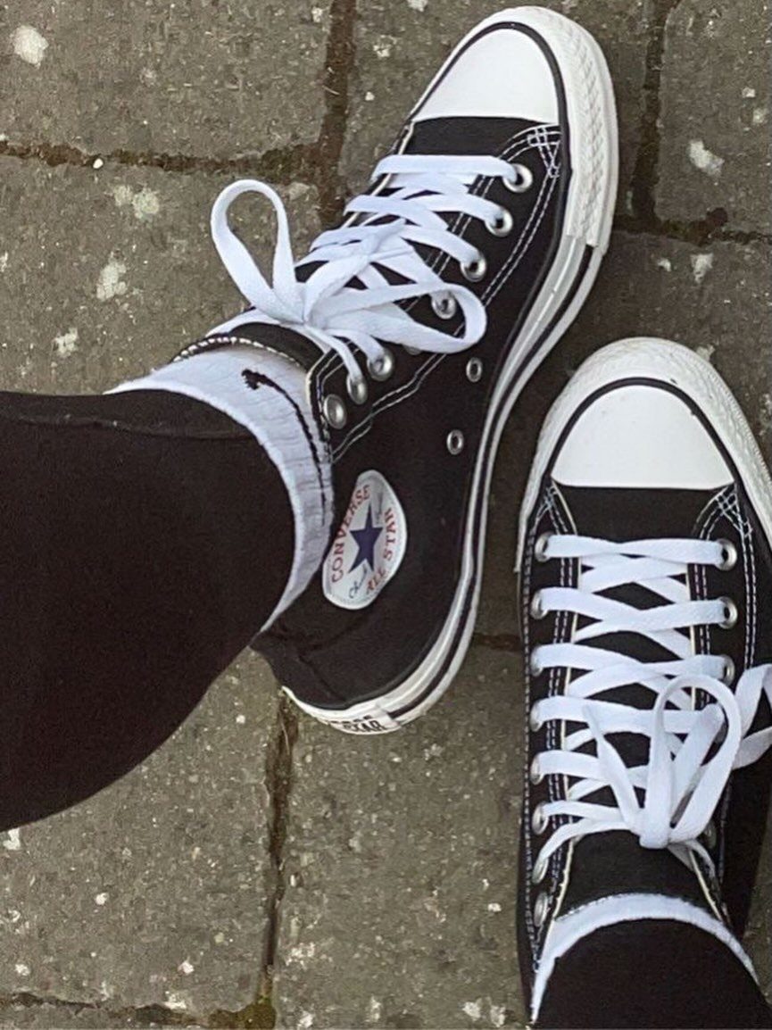 Black high-top Converse sneakers with white laces on a grey stone pavement.