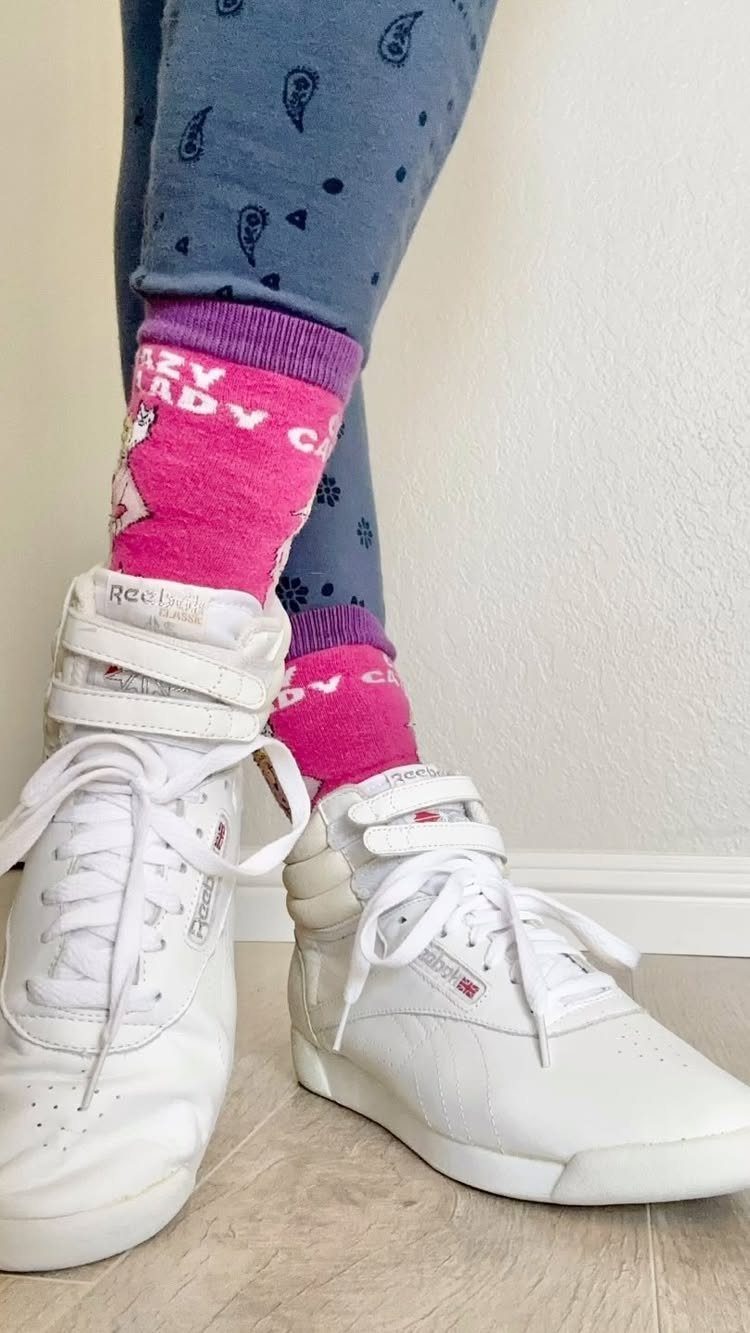 White Reebok Freestyle Hi sneakers worn with pink socks and blue patterned leggings.